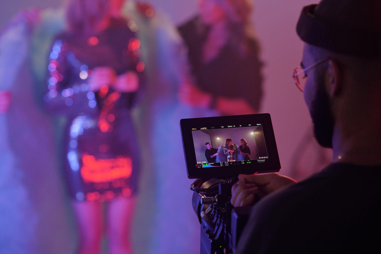 Closeup of director monitoring scene on camera display during video shoot with blurred background of performers